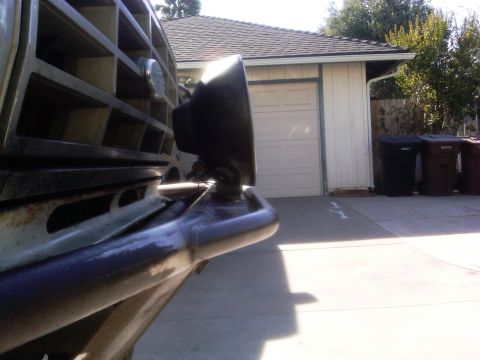 1986 Ford Bronco - Close-up view of a vehicle's front bumper and grille, with a garage and trash cans in the background.
