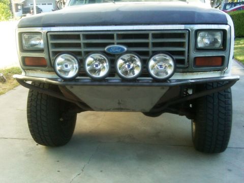 1986 Ford Bronco - Front view of a Ford Bronco showing its grille, headlights, and custom bumper with lights. The Ford logo is visible on the grille.