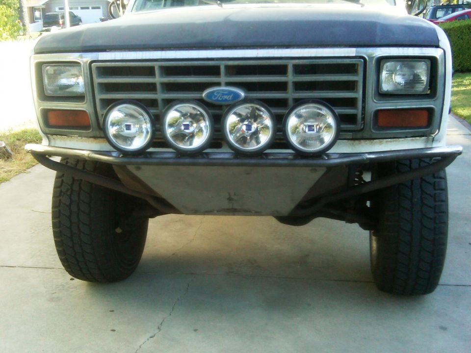 Front view of a Ford Bronco with a custom bumper and four driving lights mounted above it. The grille has a Ford logo