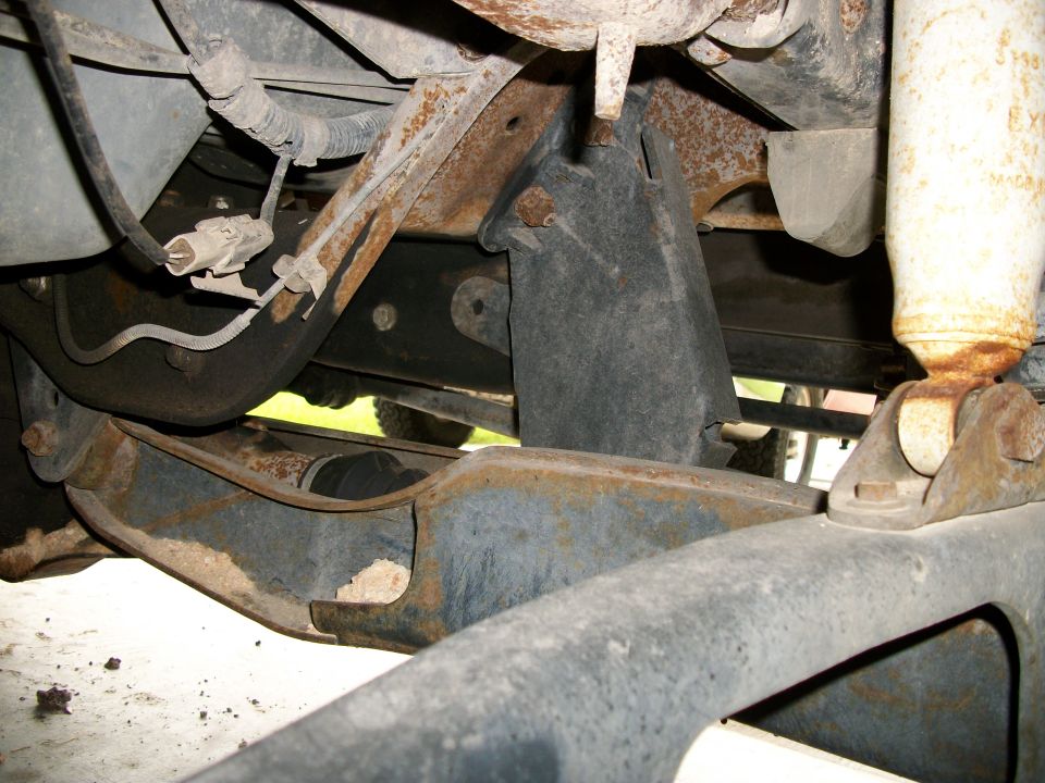 Close-up of rusty vehicle suspension parts, including a shock absorber and various metal brackets and arms
