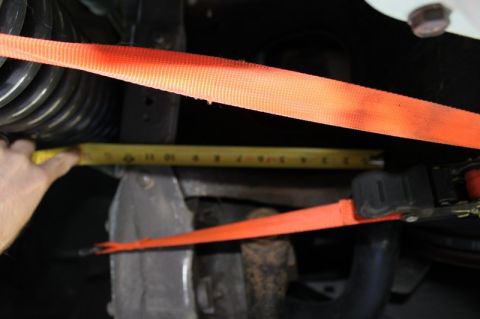 1987 Ford Bronco - Measuring suspension component with a tape measure and ratchet strap.