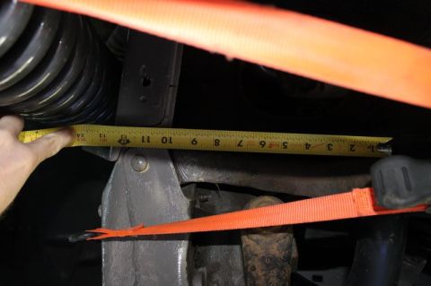 1987 Ford Bronco - A tape measure is used to measure a vehicle's suspension component, with orange straps securing the area.