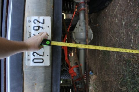 1987 Ford Bronco - A measuring tape is used to measure the width of a vehicle's rear axle, with a license plate in the foreground.
