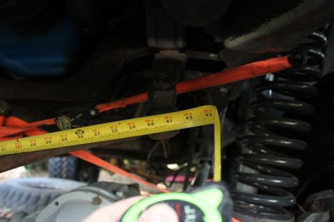1987 Ford Bronco - Measuring suspension components with a yellow tape measure, showing a coil spring and red strap.