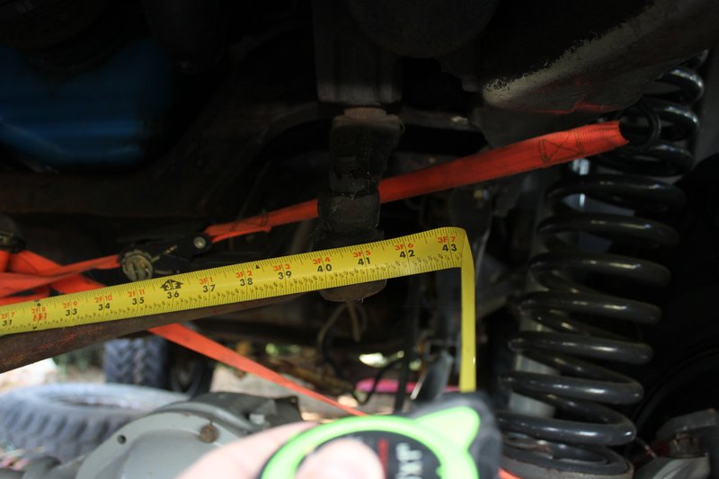 Measuring suspension components with a yellow tape measure, showing a coil spring and red strap