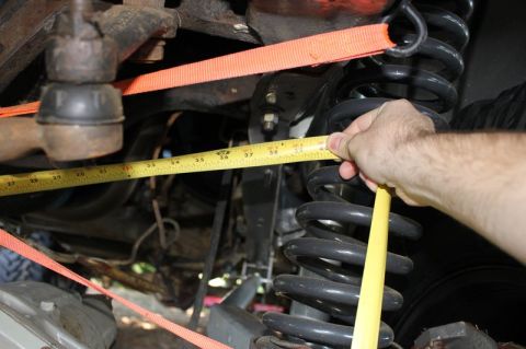1987 Ford Bronco - A tape measure is used to measure the suspension coil of a vehicle's undercarriage.