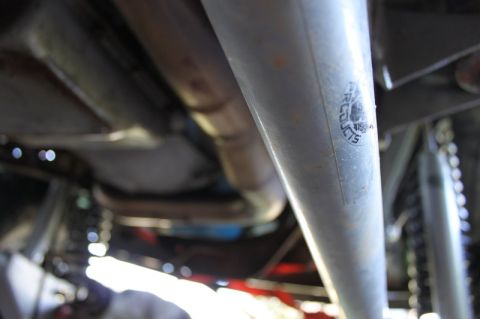 1987 Ford Bronco - A close-up view of the undercarriage of a vehicle, showing various mechanical components and a sticker on a pipe.