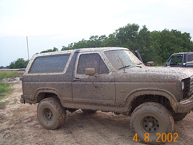 Mud-covered SUV, 3/4 front view, showing side and front fender. Another vehicle is partially visible to the right