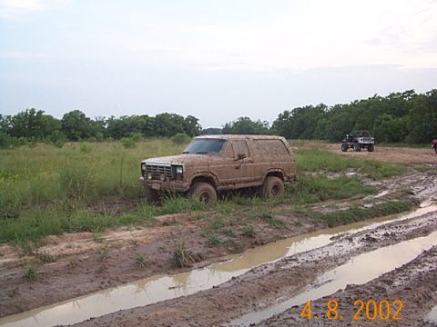 1986 Ford Bronco - This 1986 Ford Bronco is shown off-roading through a muddy track, with another vehicle visible in the distance.