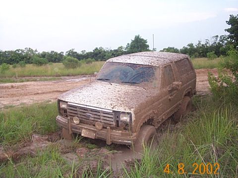 1986 Ford Bronco - This SUV is deeply stuck in the mud, with its tires submerged and mud splattered all over its body.