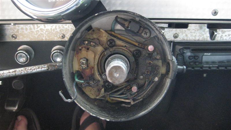 Disassembled steering column with exposed wiring and ignition components. A Pyle car stereo is visible to the right