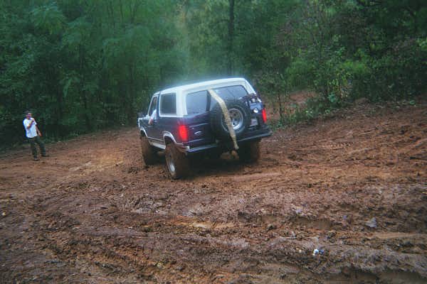 Blue and white Ford Bronco with rear tire carrier in deep red clay mud ruts