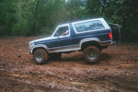 1986 Ford Bronco - This Ford Bronco is navigating a muddy trail with its tires deep in the muck.