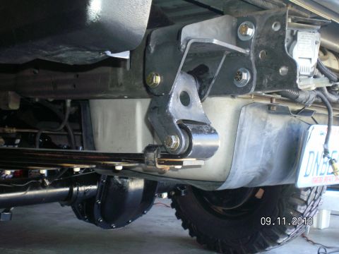 1996 Ford Bronco - Underbody shot from below a truck showing a heavy steel drop bracket bolted to the frame with yellow zinc hardware, mounting a radius arm a…