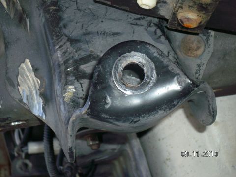 1996 Ford Bronco - Underside close-up of a black stamped-steel leaf spring hanger bracket welded to the frame rail, with the empty bolt hole and its sleeve ex…
