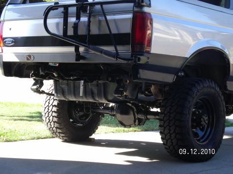 1996 Ford Bronco - Low rear three-quarter shot of a lifted silver and gray two-tone Ford SUV on a driveway, framed to show the exposed rear suspension: painte…