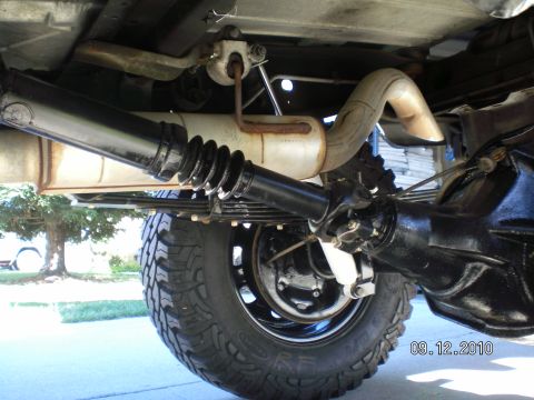 1996 Ford Bronco - Under-truck view looking at the rear of the driveshaft, black rear axle housing and leaf spring pack, with a rubber-booted slip yoke and U-…