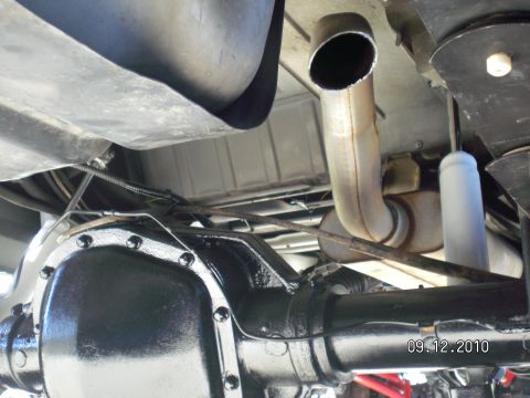 1996 Ford Bronco - Underbody view of a gloss black rear axle housing with bolted differential cover, brake lines and vent hose routed across it, below a large…