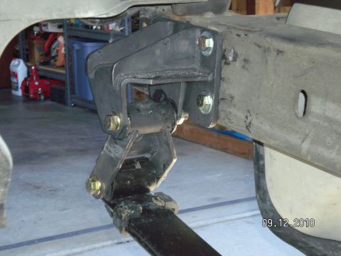 1996 Ford Bronco - Underbody view of a newly installed drop bracket bolted to the frame rail with yellow zinc hardware, holding the radius arm and a black rub…