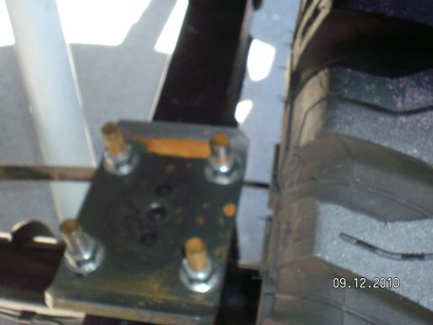 1996 Ford Bronco - Slightly blurry underbody shot of a flat steel spring perch/mounting plate held by four studs with hex nuts and washers, showing a small dr…