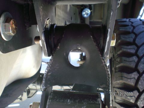 1996 Ford Bronco - Underbody shot of a black welded leaf spring shackle box bracket with an open bolt hole, mounted between the frame and a fresh weld bead, w…