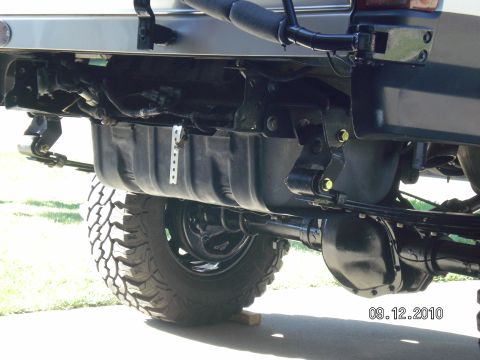 1996 Ford Bronco - Underside rear view of a lifted truck showing the black fuel tank, frame rails, leaf springs with yellow zinc shackle bolts, and the rear a…