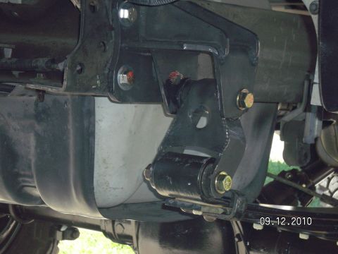 1996 Ford Bronco - Underbody view of a black welded shackle-flip bracket bolted to the frame rail with yellow zinc hex bolts, with the leaf spring eye and sha…