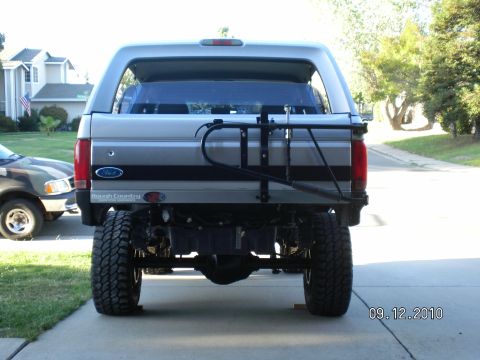 1996 Ford Bronco - This lifted Ford Bronco is equipped with a camper shell and a bike rack, seen parked next to another vehicle.
