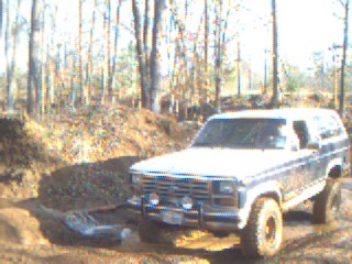 1986 Ford Bronco - A white 1987 Ford Bronco navigates a dirt path in a wooded area.
