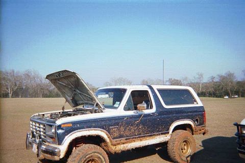 1986 Ford Bronco - This 1986 Ford Bronco is shown with its hood open, covered in mud, and parked in a field.