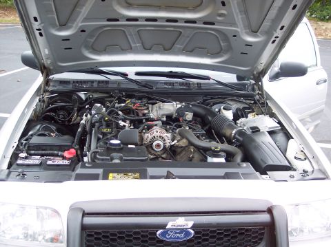 2001 Ford Crown Victoria - The engine bay of a 2001 Ford Crown Victoria is visible with the hood raised, revealing the V8 engine and the Ford emblem on the grille.