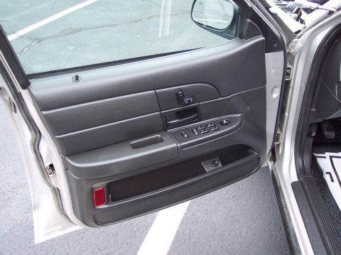 2001 Ford Crown Victoria - The interior door panel of a car shows the window controls and a storage compartment.