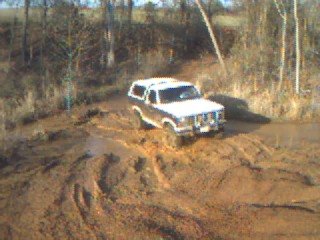1986 Ford Bronco - A white Ford Bronco navigates a challenging muddy path in an outdoor setting.