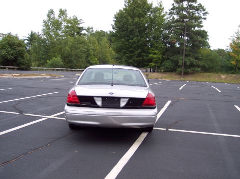 2001 Ford Crown Victoria - A silver 2001 Ford Crown Victoria is parked in a nearly empty parking lot with trees in the background.