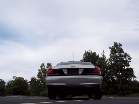 2001 Ford Crown Victoria - The rear of a silver 2001 Ford Crown Victoria is visible against a cloudy sky and trees.
