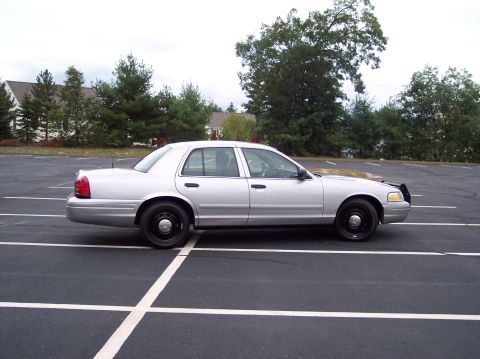 2001 Ford Crown Victoria - Side profile of a silver Ford Crown Victoria, likely a police vehicle, parked in a lot.