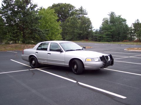 2001 Ford Crown Victoria - Silver 2001 Ford Crown Victoria police car with a push bumper is parked in an empty lot.