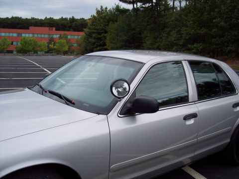 2001 Ford Crown Victoria - A silver 2001 Ford Crown Victoria police car is parked in an empty lot, showing its side profile and spotlight.