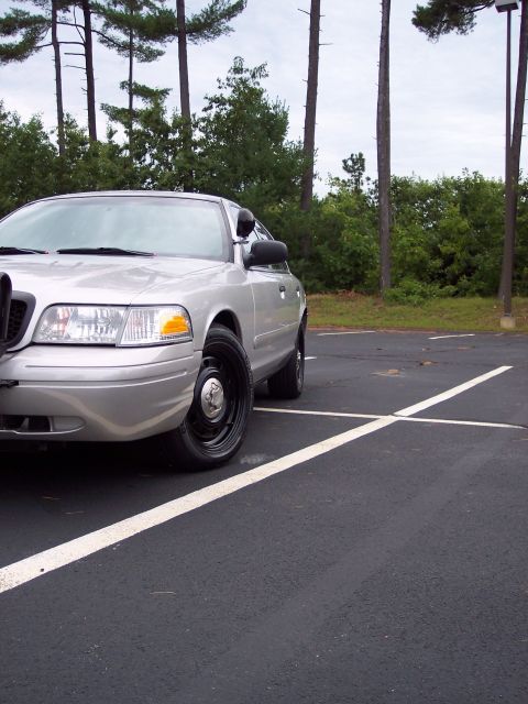 2001 Ford Crown Victoria - Silver 2001 Ford Crown Victoria police car parked in a lot with trees in the background.