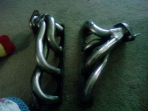 1995 Ford Bronco - Two exhaust manifolds are shown on a carpeted surface, with a Supermotors.net watermark in the lower right corner.