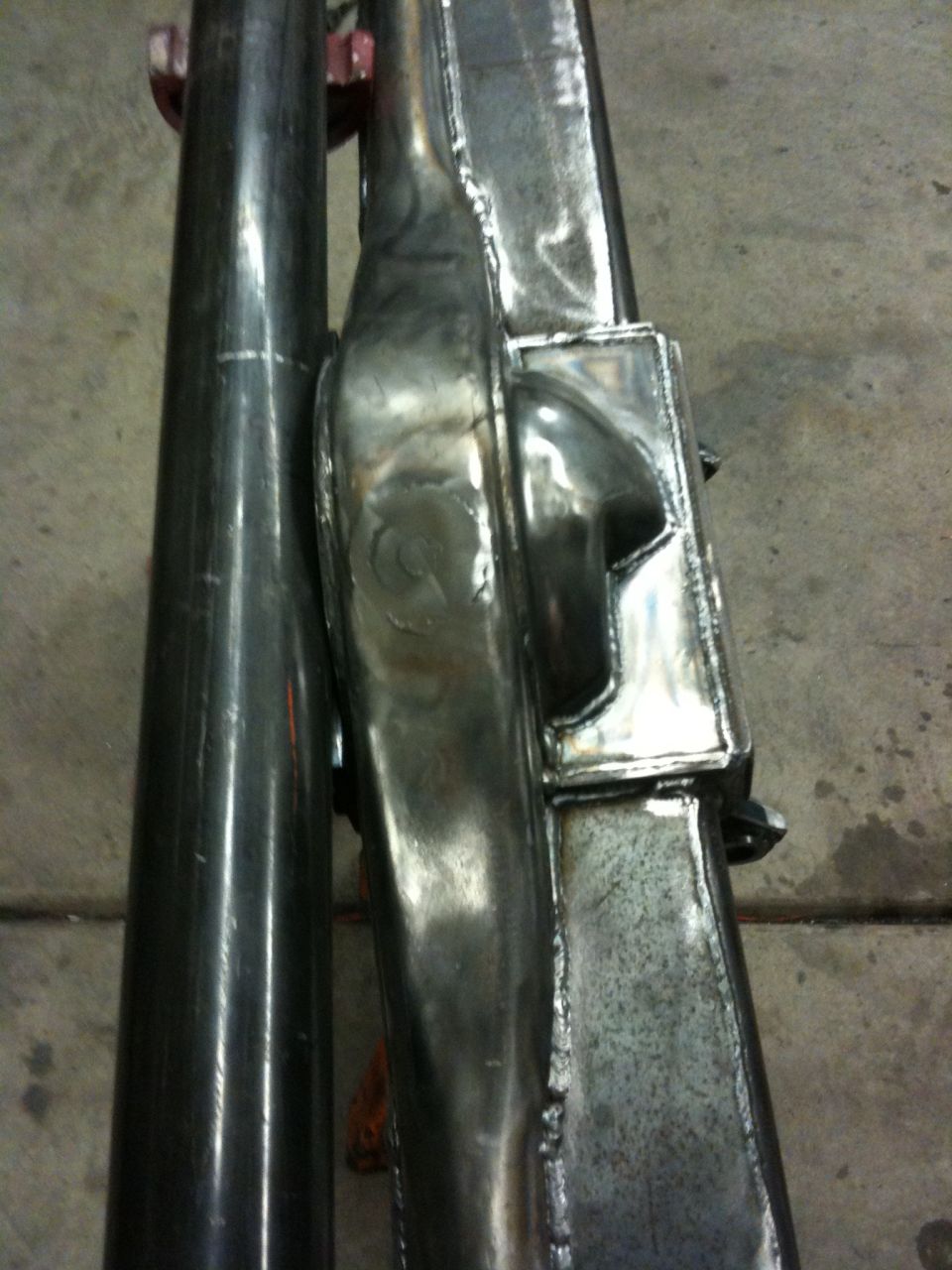 Close-up of a shiny, welded metal frame part with a pipe next to it