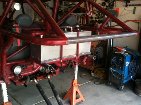 Suzuki Samurai - Rear of a red tube-chassis rock buggy up on jack stands in a home garage during fabrication, with a bare aluminum fuel cell mounted behind…