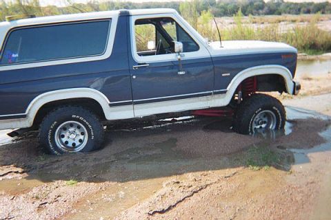 1986 Ford Bronco - This 1986 Ford Bronco is navigating a muddy, watery terrain, with its tires partially submerged.