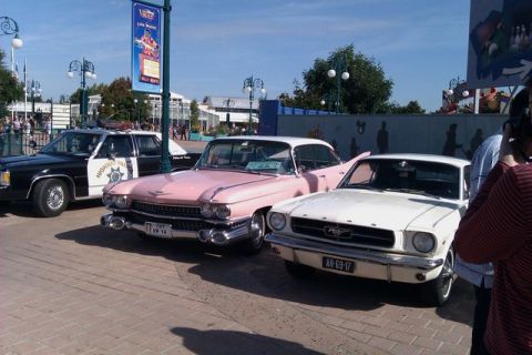 1991 Ford LTD Crown Victoria - A police car, a pink Cadillac, and a white Ford Mustang are parked together on a sunny day.