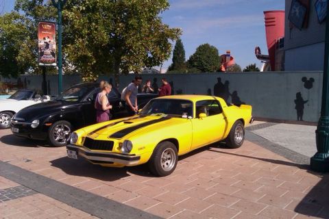 1991 Ford LTD Crown Victoria - A yellow 1977 Chevrolet Camaro is parked on a brick surface with people nearby.
