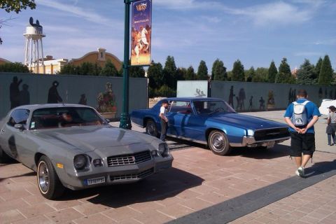 1991 Ford LTD Crown Victoria - Two classic cars are parked on a sunny day with a mural and a water tower in the background.