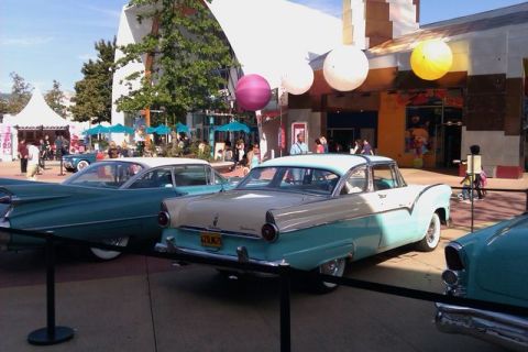 1991 Ford LTD Crown Victoria - Two classic two-tone sedans, a 1955 Ford and a teal Cadillac, are parked outside a building.