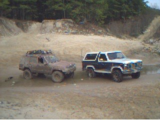 1986 Ford Bronco - Two SUVs are parked on a dirt road, with one appearing to be a 1986 Ford Bronco.