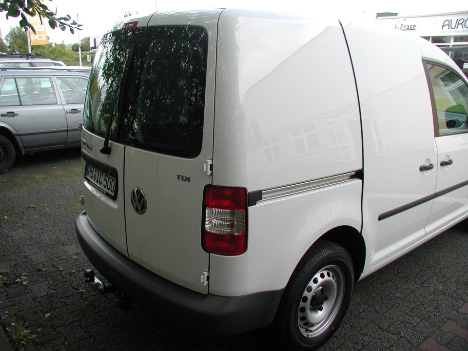 White VW Caddy panel van rear, with tow bar and German plate, parked in a lot.
