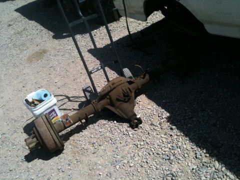 1966 Ford Bronco - A disassembled rear axle assembly sits on a gravel surface next to a white bucket containing tools and cleaning supplies.
